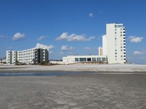 A beachfront hotel with multiple buildings, including a tall white tower and a shorter building with balconies.