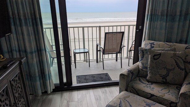 Un balcón con vista a la playa, un sofá, una silla y una mesita.