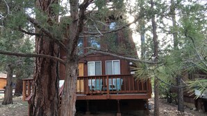A cabin with a wooden deck, large windows, and a view of the surrounding forest. - Sugarloaf Cabin sweet cabin (Big Bear)