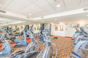 Un gimnasio con máquinas de cardio variadas, una alfombra estampada y un muro con espejos.