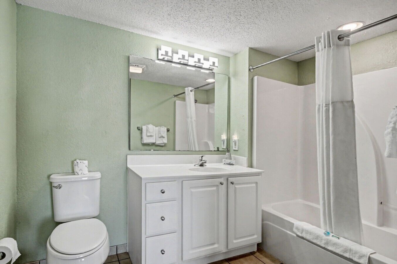A bathroom with a toilet, a sink with a mirror, and a shower area.
