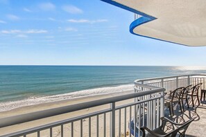 A balcony with a view of the beach and ocean, featuring a railing and seating area.