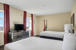 Ein Hotelzimmer mit zwei Betten, einem Fernseher auf einer Kommode, einem Spiegel und einer Lampe.