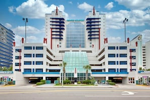 A multi-story hotel with a central glass facade, multiple parking levels, and a prominent entrance. - 4BR/3BA, Sleeps 16, Large Oceanfront, Balcony (Myrtle Beach)