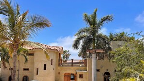 A courtyard with a building featuring a tiled roof, a wooden gate, and palm trees. - Magical Beach House with Unforgettable Ocean Views (Todos Santos)