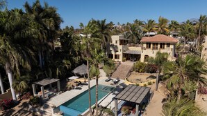 A resort with a swimming pool, palm trees, and a thatched-roof structure. - Magical Beach House with Unforgettable Ocean Views (Todos Santos)