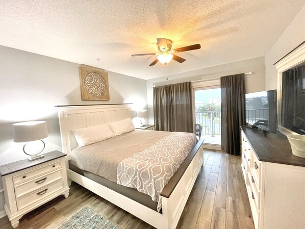 A bedroom with a bed, bedside table, lamp, ceiling fan, and a TV.