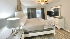 Habitación de hotel con cama, televisor, ventilador de techo y vistas al exterior.