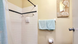 A bathroom with white tiled walls, a shower area, a toilet, a towel rack, and a mirror with a decorative frame. - 50 Steps to Beach Villa Hot Tub 1bd modern cottage (Bradenton Beach)
