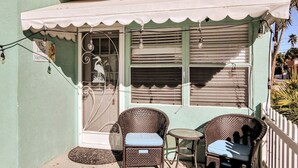 Un petit espace extérieur aménagé avec des chaises et une table en osier, un auvent blanc et une enseigne indiquant « La Petite Sirène ».