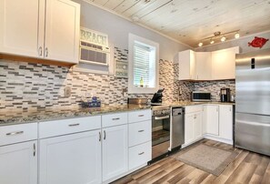 A modern kitchen with white cabinets, a stainless steel refrigerator, and a tiled backsplash. - 50 Steps to Beach Villa Hot Tub 1bd modern cottage (Bradenton Beach)