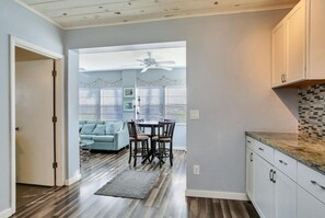 A modern kitchen with white cabinets, a granite countertop, and a dining area with a table and chairs. - 50 Steps to Beach Villa Hot Tub 1bd modern cottage (Bradenton Beach)