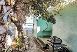 Un étroit sentier extérieur mène à un bâtiment verdoyant où se trouve un barbecue.