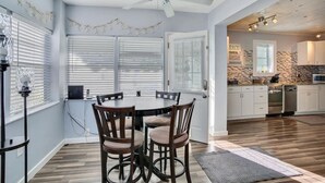 A dining area with a round table and chairs, a ceiling fan, and a kitchen in the background. - 50 Steps to Beach Villa Hot Tub 1bd modern cottage (Bradenton Beach)
