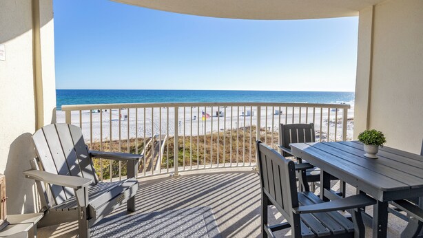 A balcony with a view of the beach, a table, and two Adirondack chairs. - Gorgeous Recently Updated 3rd Floor Direct Beachfront Condo Perfect Location (Gulf Shores)