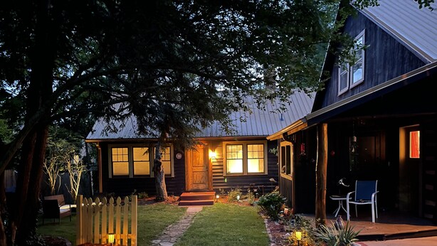 Uma casa com varanda iluminada, entrada por um caminho de cascalho e pequeno gramado.