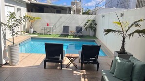 A backyard with a swimming pool, two lounge chairs, a small table, and a sofa.