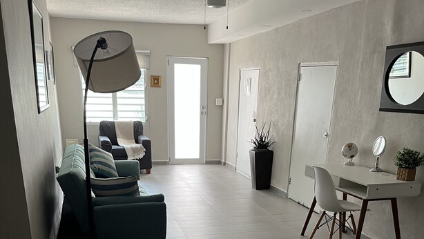 A spacious living area with a sofa, a dining table with chairs, a standing lamp, and a potted plant.