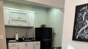 A compact kitchen with white cabinets, a black refrigerator, and a dining table with chairs.