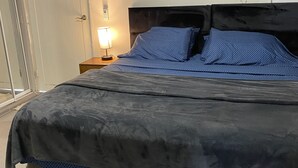 A modern bedroom with a bed, a nightstand, a lamp, and an air conditioning unit.