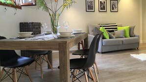 A dining area with a wooden table set for two, surrounded by black chairs. There is a grey sofa with patterned cushions in the background.