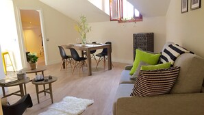 A cozy living room with a high ceiling, a dining area with a wooden table and chairs, a sofa with patterned cushions, and a white furry rug. - PLAZA MAYOR-SOL (Madrid)