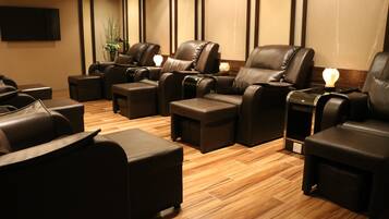 A massage room with several leather massage chairs, wooden flooring, and a wall-mounted TV.