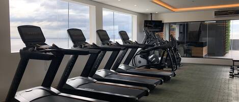 Un gimnasio con cintas de correr alineadas contra una pared con ventanas amplias que dan al cielo.