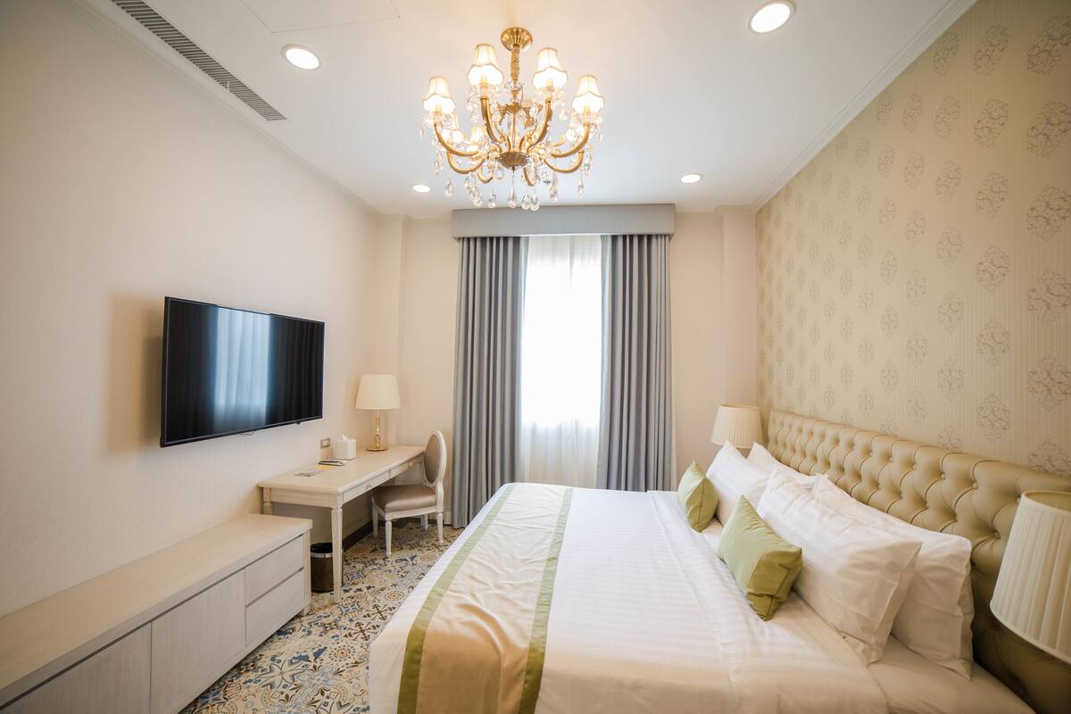 Une chambre d’hôtel équipée d’un lit, d’un bureau, d’une chaise, d’une télévision et d’un lustre.