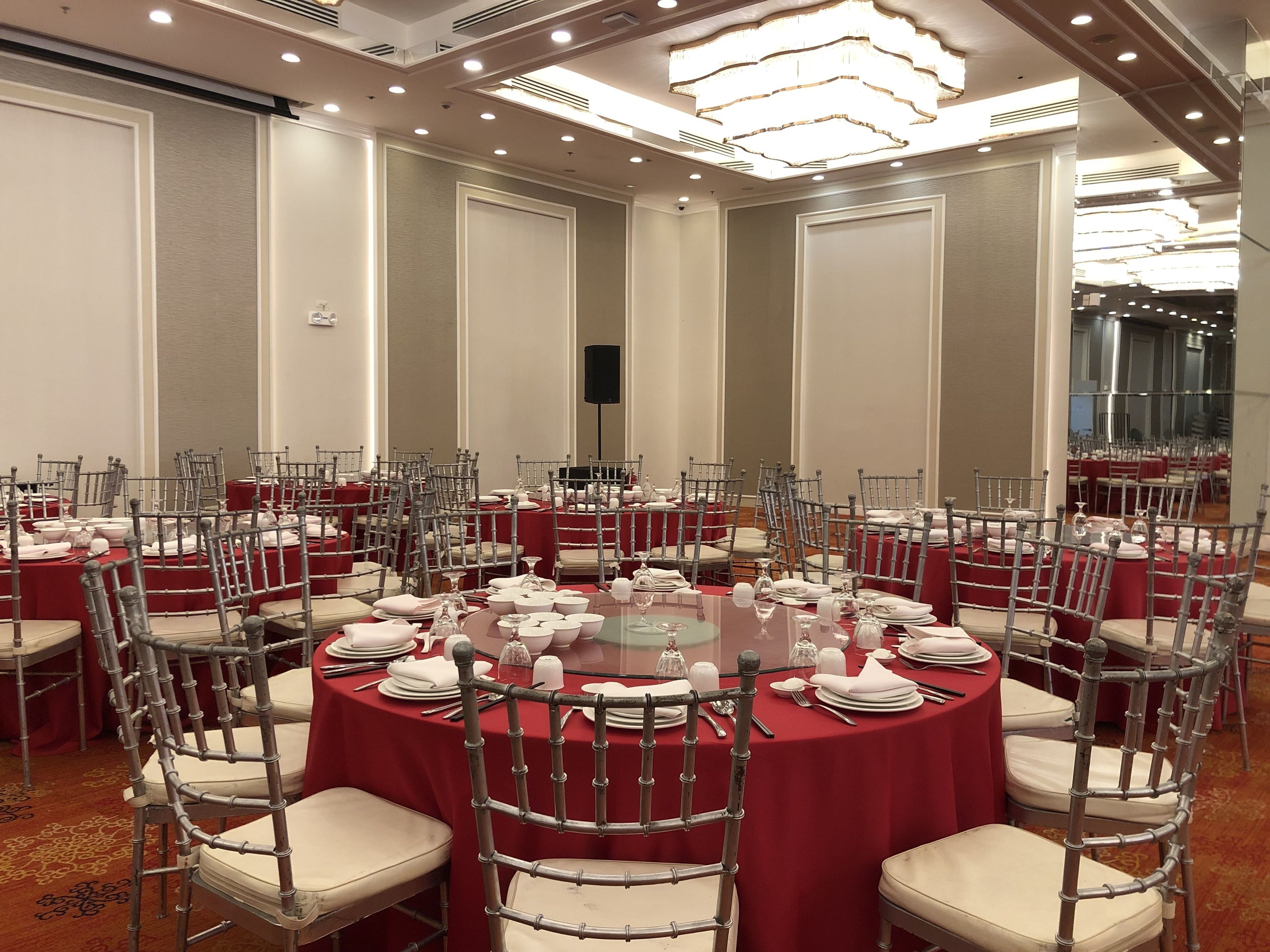 Un salón de conferencias con mesas redondas, manteles rojos y sillas metálicas.