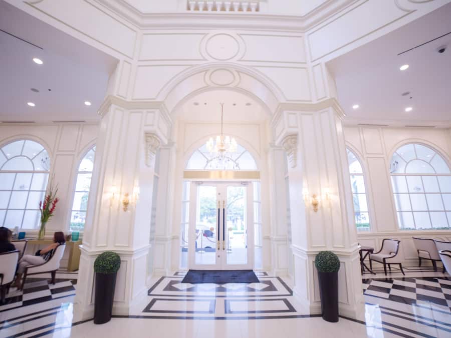 A grand lobby with a checkered floor, large arched windows, and a chandelier.