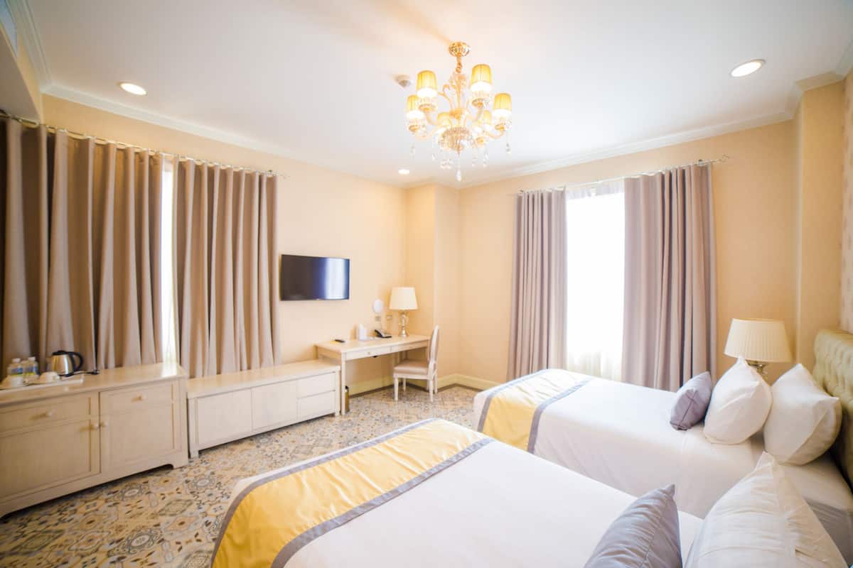 Une chambre d’hôtel avec deux lits, un bureau, une chaise, une télévision et un lustre.
