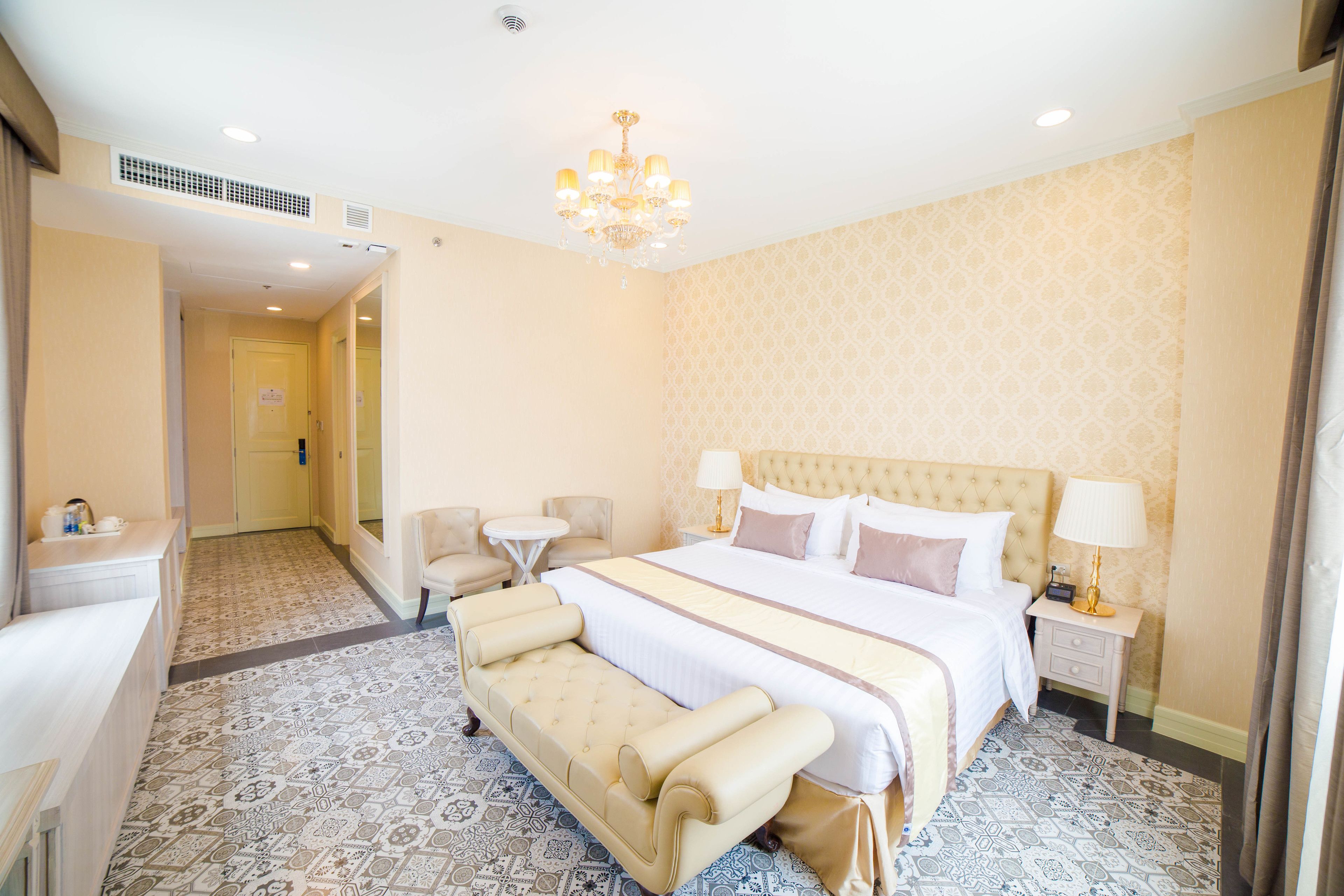A hotel room with a large bed, a sitting area with a sofa and armchairs, a small table, and a nightstand with a lamp.