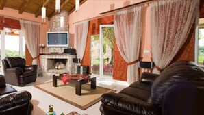 A living room with leather sofas, a fireplace, a TV, and large windows with curtains. - “Private Luxury Estate with Pool, Tennis & Cinema” (Gouvia)