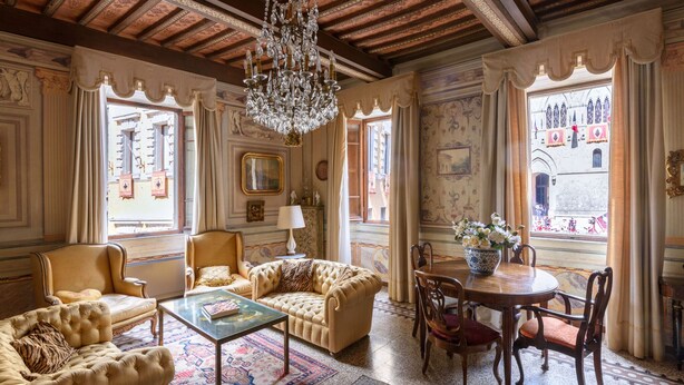 Ein geräumiger Raum mit einem großen Chandelier, einer verzierten Decke und Blick auf ein Gebäude durch die Fenster.