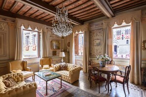 A spacious room with a large chandelier, ornate ceiling, and a view of a building through the windows.