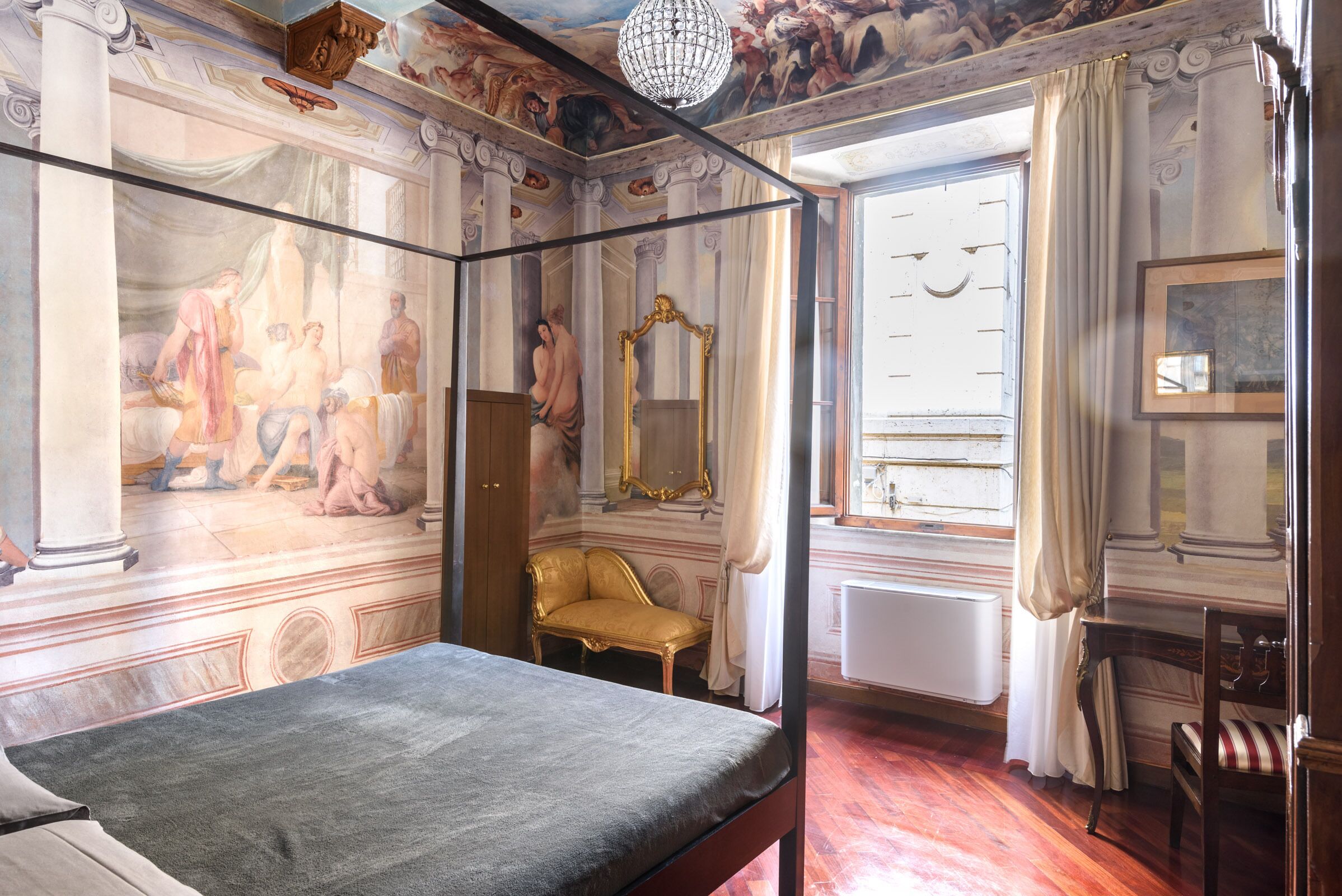 A room with a bed, a golden chair, a large mirror, and a ceiling mural.