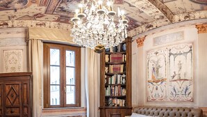 Ein klassisches Schlafzimmer mit einem großen Bett, einer Chandelier, einer Bücherwand und aufwändigen Deckenverzierungen.