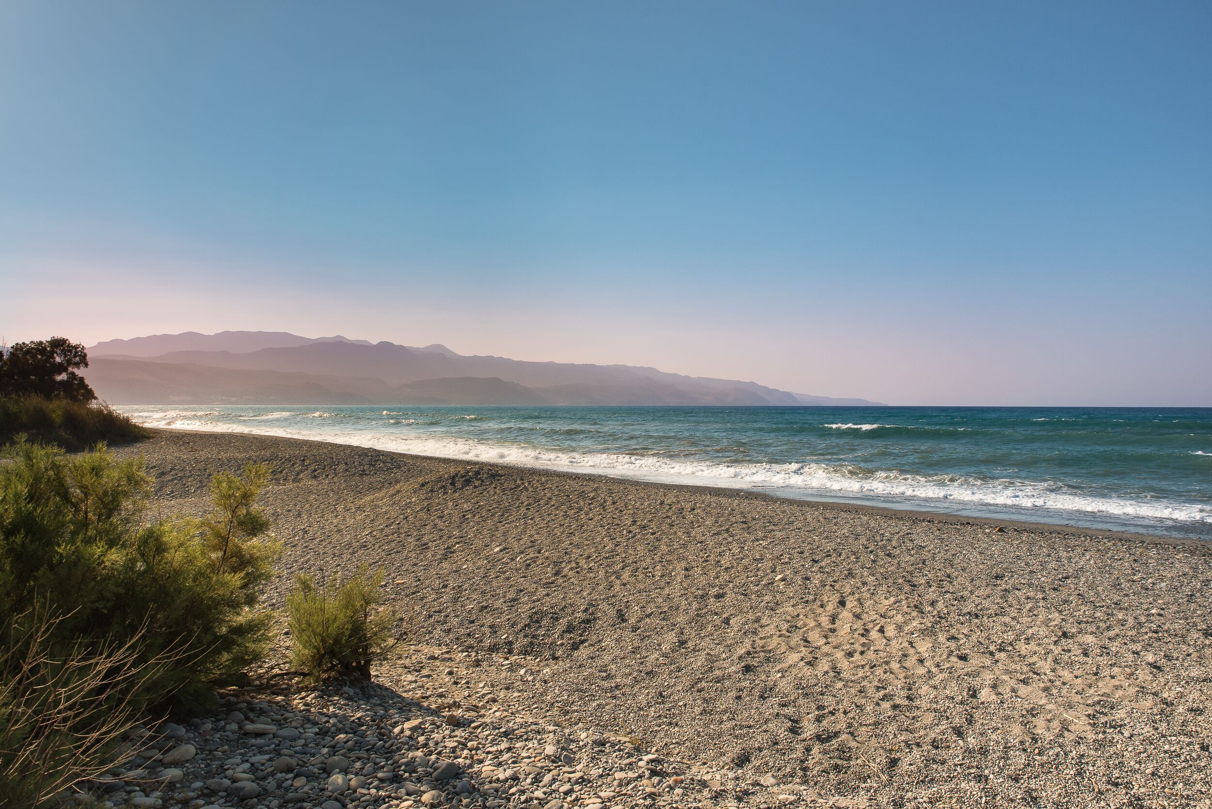 A rocky beach with a clear view of the ocean and distant mountains.