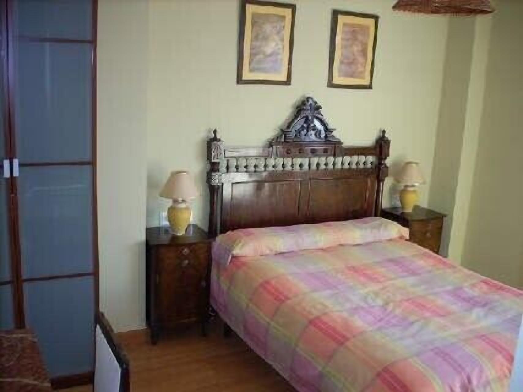 Un dormitorio con una cama de madera, dos lámparas de noche y dos cuadros en la pared.