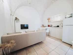 A modern kitchen with a built-in oven, a dining area with a white chair, and a TV mounted on the wall.