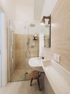 A modern bathroom with a glass-enclosed shower, a white sink, and a wooden stool.