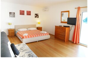 Quarto com cama, mesas de cabeceira, cômoda, televisão e janela com cortinas.