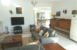 Sala de estar com televisão de tela plana, sofá, mesa de centro e área de jantar com mesa de bilhar.