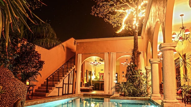 A pool area with a staircase leading to an upper level, surrounded by tropical plants and architectural columns. - Ochenta Y Dos an urban bed & breakfast (Mérida)