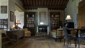 A rustic living room with wooden floors, a fireplace, bookshelves, a dining table, and a sofa.