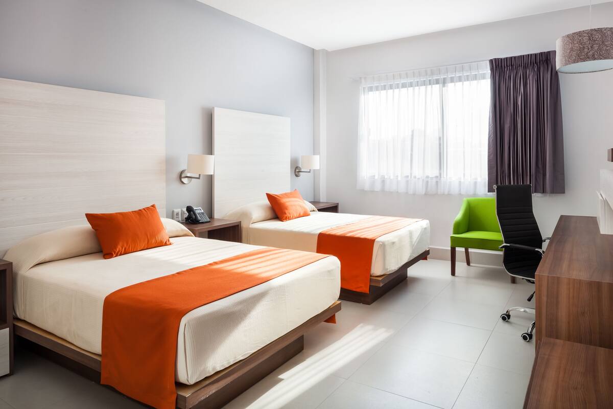 Hotellihuone, jossa on kaksi sänkyä, työpöytä, tuoli ja ikkuna, jossa on verhot.