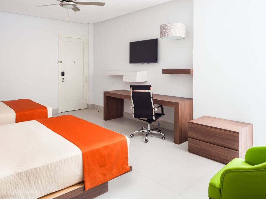 Habitación de hotel con una cama, un escritorio, una silla, un televisor y un sillón verde.