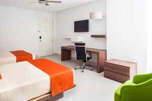 Habitación de hotel con una cama, un escritorio, una silla, un televisor y un sillón verde.