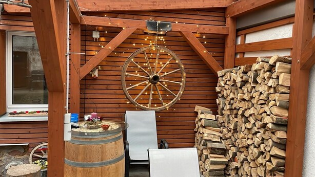 Una cabaña rústica de madera con una rueda grande, un barril y una pila de leña.
